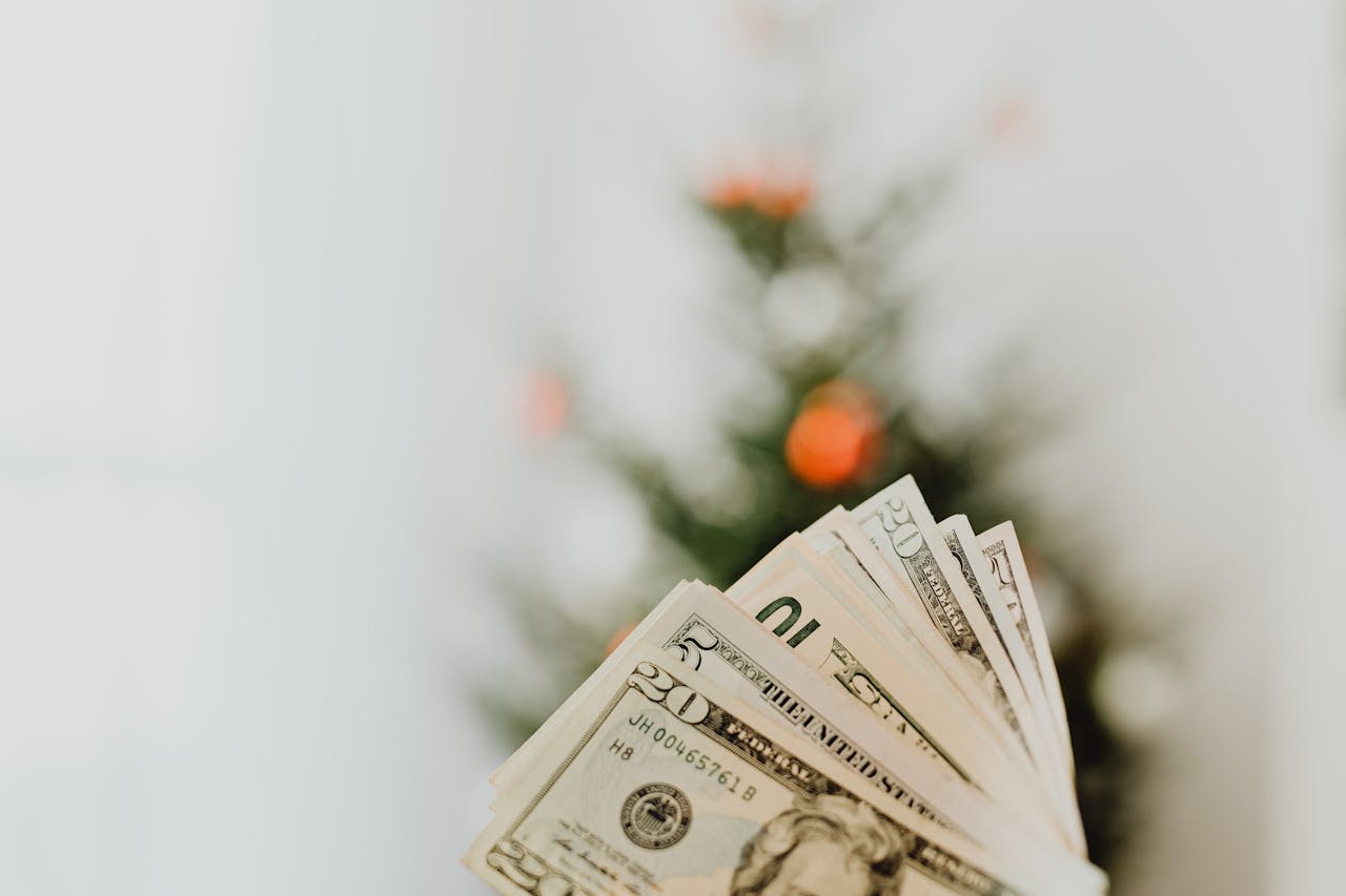A close-up shot of US dollar banknotes with a blurred tree in the background, suggesting festive savings.